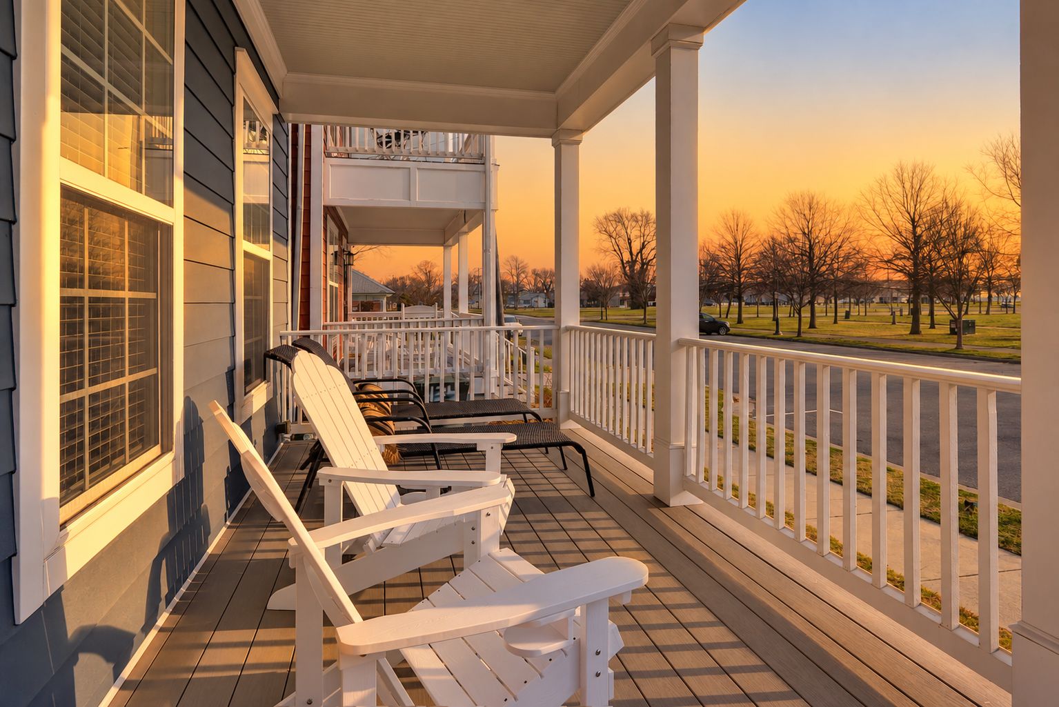 Eine überdachte Veranda mit weißen Geländern, zwei Adirondack-Stühlen und einer Bank.