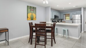 Una cocina moderna con armarios grises, electrodomésticos de acero inoxidable y un comedor con sillas de madera y un taburete azul claro.