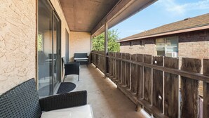 Un balcón techado con mobiliario de mimbre y una valla de madera.