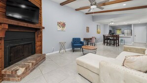 Amplia sala de estar con chimenea, ventilador de techo y comedor al fondo.