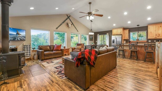 A spacious living area with a fireplace, leather sofas, a dining area, and a kitchen with wooden cabinets and bar stools. - Moose Mountain Lodge Above Park City (Summit County)