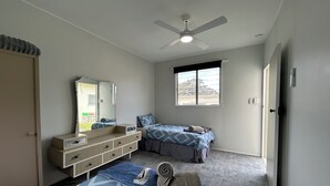 A bedroom with a bed, a dresser, a mirror, a ceiling fan, and a window.