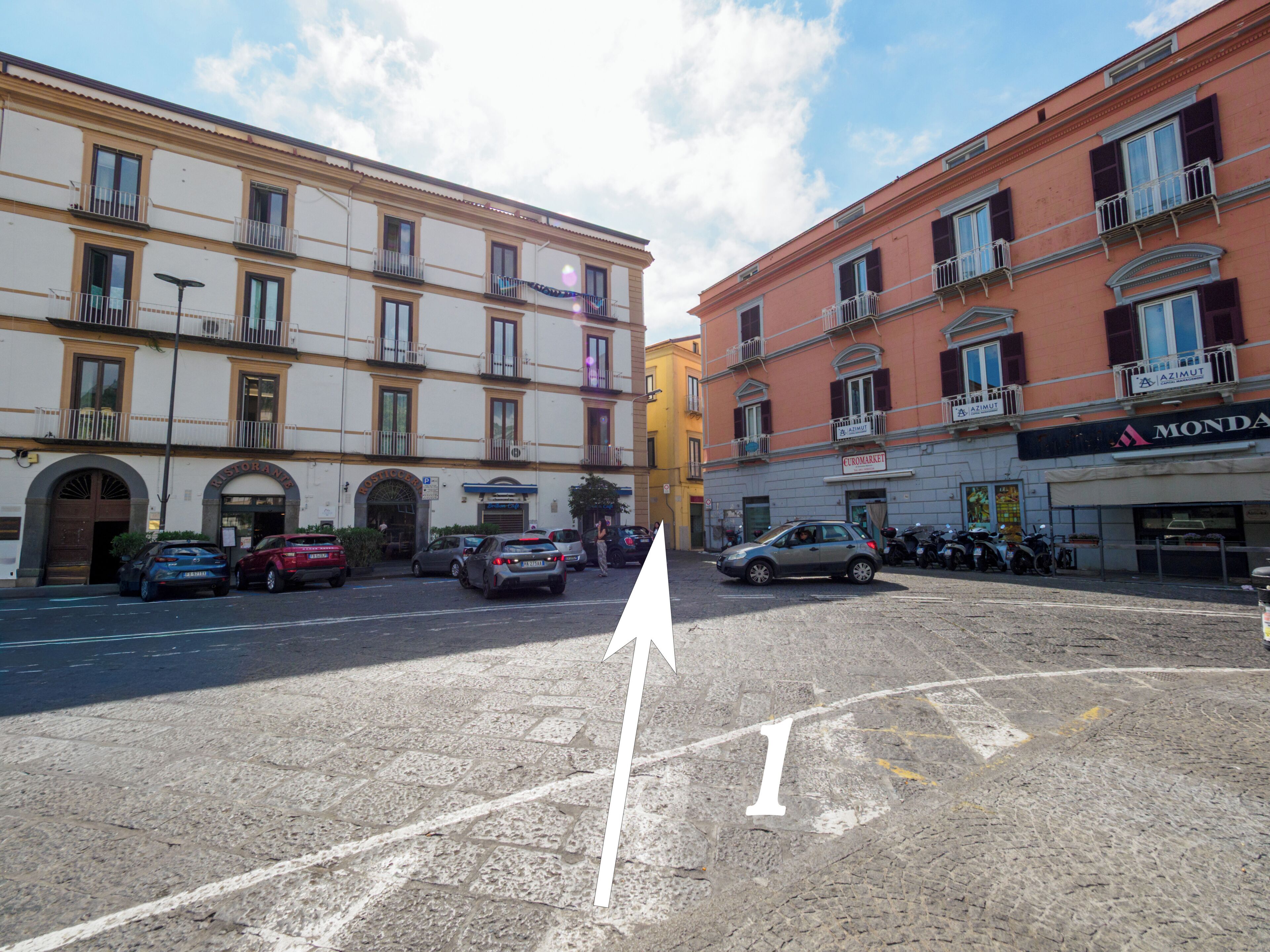 A street with buildings, cars, and a white arrow pointing straight ahead.