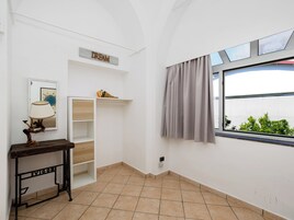 Um quarto com parede branca, janela com cortinas, luminária, prateleira com um aviso e piso de azulejos.