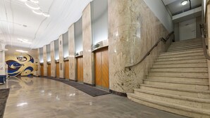 Una hall moderna e luminosa, con pavimento in marmo, parete curva ornata da un murale decorativo e una scalinata che conduce a un piano superiore.
