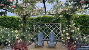 En have med et pergola overdækket af blomster, to Adirondack-stole og et espalierhegn i baggrunden.