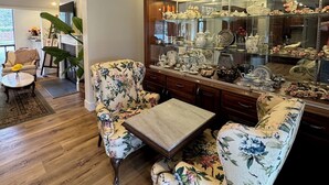 En stue med en blomstret sofa, et sofabord og et glasmontre fyldt med pynt.