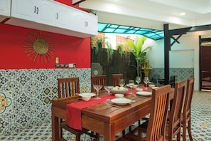 A dining area with a wooden table set for four, surrounded by chairs. There is a red tablecloth, a decorative wall with a sun motif, and a patterned tile floor. - Spacious 8-Bedroom Villa in fabulous Krong Siem Reap with Private Pool (Krong Siem Reap)
