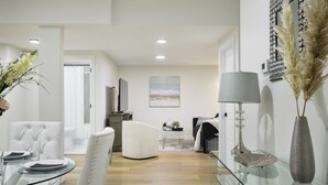 Ein modernes Wohnzimmer mit einem Glastisch, weißen Ledersesseln, einem grauen Sofa und einer dekorativen Lampe.