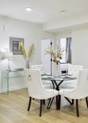 A dining area with a glass table, white upholstered chairs, a vase with flowers, and a decorative mirror on the wall. - Modern & Elegant Executive Suite near Refinery Row. Office Desk + Kitchen (Edmonton)
