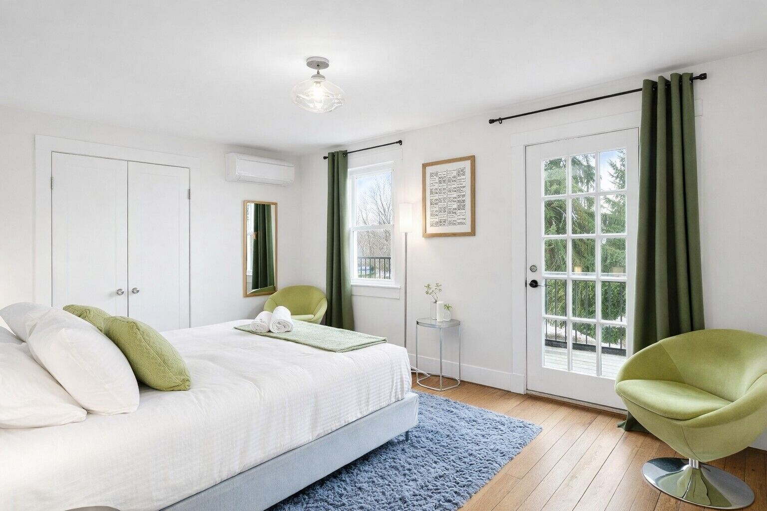 A bedroom with a bed, a chair, a small table, a mirror, a door, and a window.