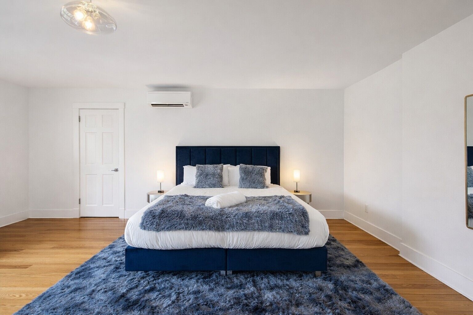 Une chambre à coucher comprenant un lit, des tables de chevet, un appareil de climatisation, une porte et un luminaire.