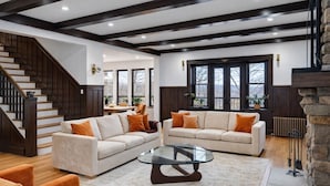 Amplia sala de estar con un sofá modular grande, una mesa de centro de vidrio y una escalera con barandales de madera oscura.