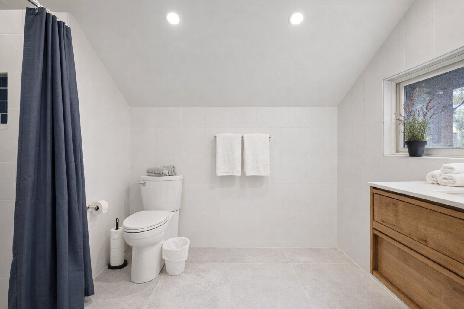 A modern bathroom with a toilet, two towels, a shower curtain, and a window with a plant.
