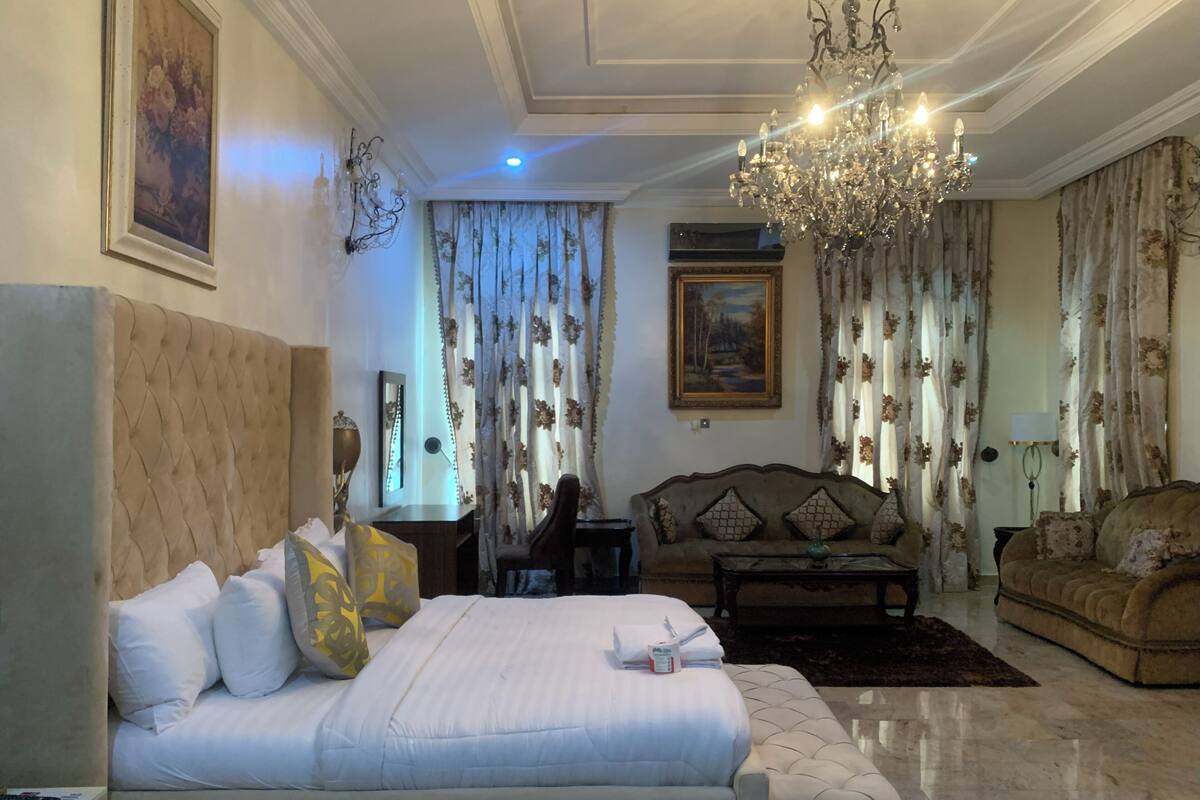 A spacious bedroom with a large bed, a sitting area with a sofa, and a chandelier.