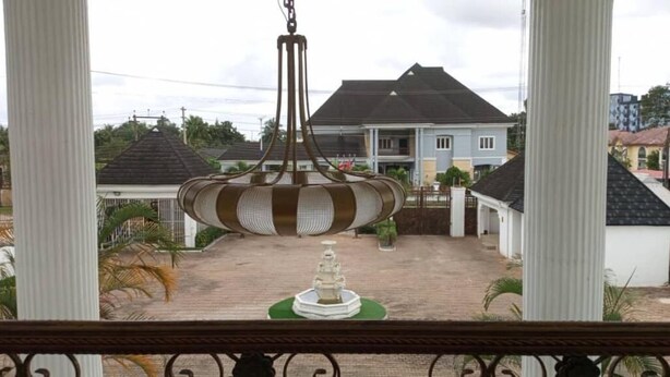 Une vue depuis un balcon, avec une lampe suspendue, une fontaine blanche et une maison en arrière-plan.