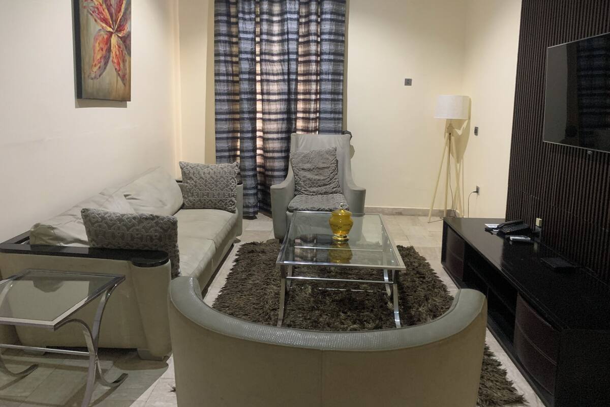 A living room with a sofa, armchair, glass coffee table, and a TV.