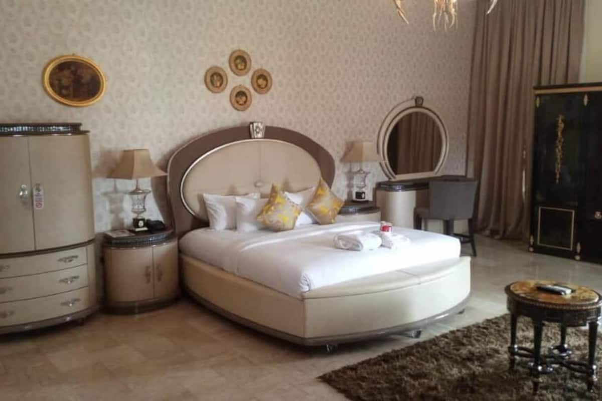 A bedroom with a large bed, a wardrobe, a nightstand, a mirror, and a small table.