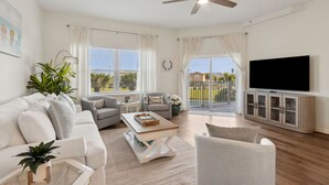 A spacious living room with a ceiling fan, a flat-screen TV, and a balcony with a view. - Ocean Park 118 - Hosted by Moore AI Rentals (Fernandina Beach)
