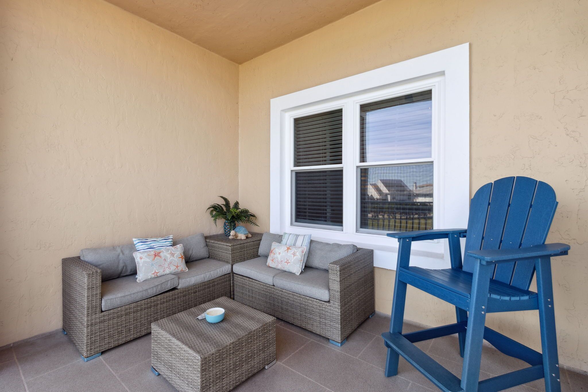 Un patio con rincón que tiene un sofá seccional gris, una silla Adirondack azul y una mesita con un cuenco.