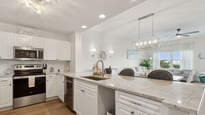A modern kitchen with white cabinetry, stainless steel appliances, a granite countertop, and a ceiling fan. - Ocean Park 118 - Hosted by Moore AI Rentals (Fernandina Beach)