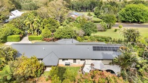A modern house with a solar panel roof, surrounded by lush greenery and hills in the background.