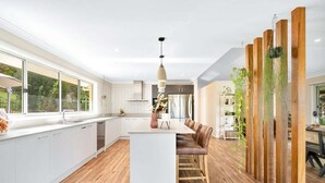 A modern kitchen with white cabinets, a central island, and a dining area with brown chairs.