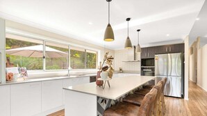 A modern kitchen with a large island, bar stools, pendant lights, and a view of the outdoors.