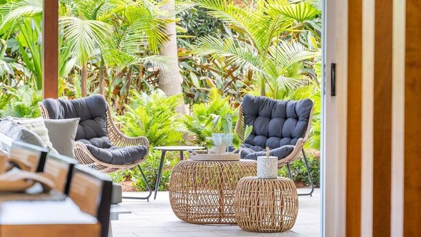 A patio area with wicker furniture and a view of lush greenery.