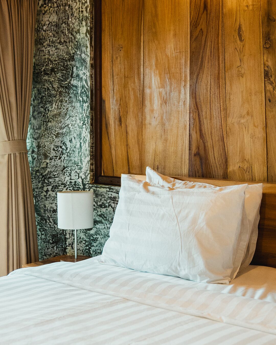 Ein Bett mit weißer Bettwäsche, einem Holz-Kopfteil, einer Lampe und einer strukturierten Wand.