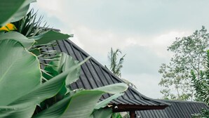 A traditional building with a curved roof, surrounded by lush greenery and a concrete pathway. - Mina Baturiti Hotel & Resto (Baturiti)