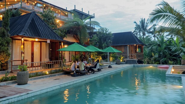 A poolside area with outdoor seating and umbrellas, surrounded by lush greenery and a building with a modern design. - Mina Baturiti Hotel & Resto (Baturiti)