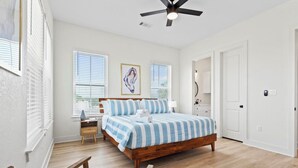 A bedroom with a wooden bed, a ceiling fan, and a bedside table with a lamp. - New! Galveston Retreat -Sleeps 10-EV Charger -Fast WiFi -Near Beach (Galveston)