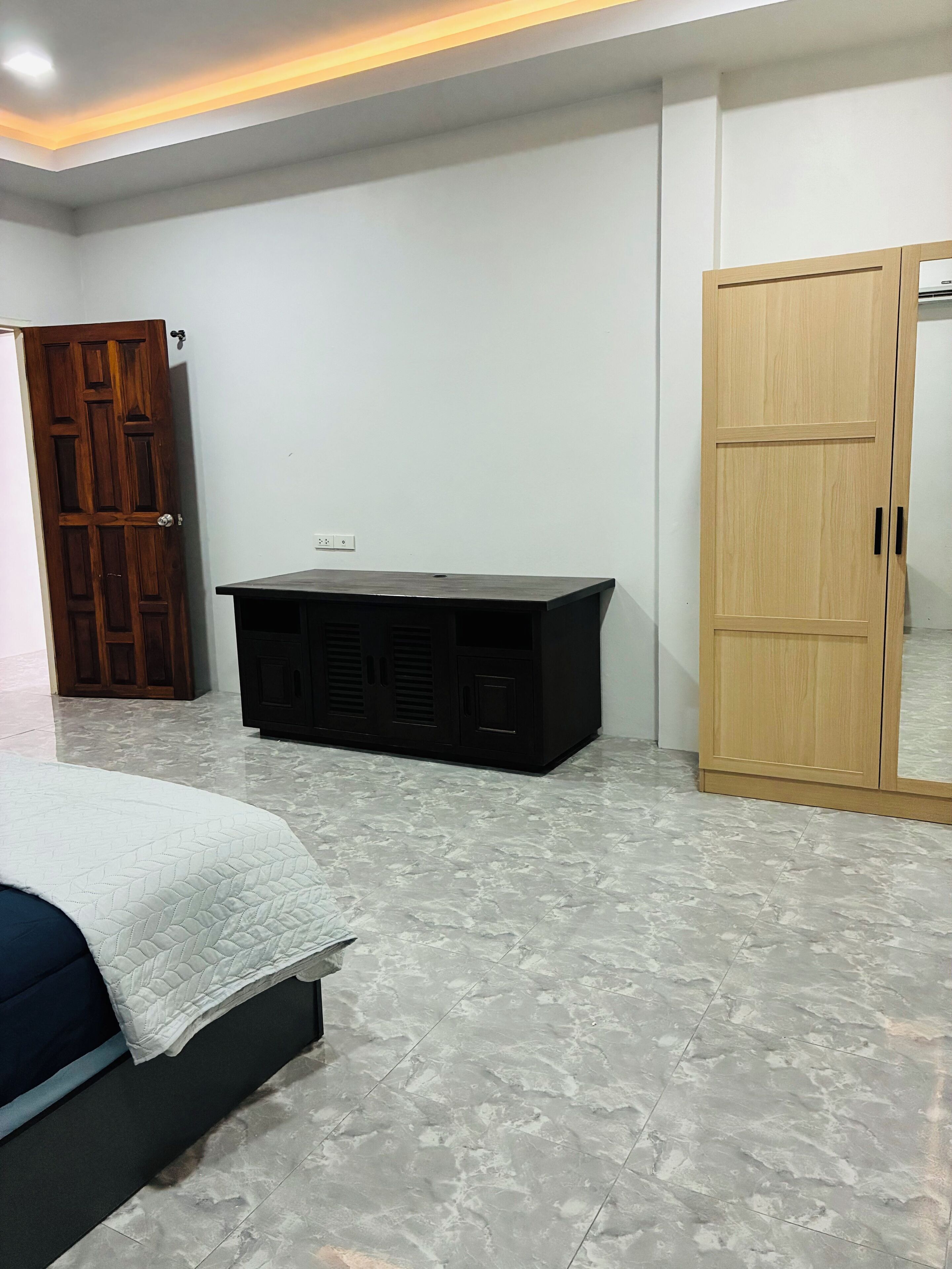 A bedroom with a bed, a wooden wardrobe, and a black cabinet.