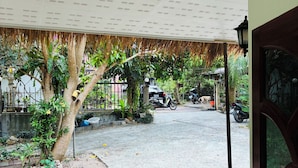 A covered outdoor area with a concrete floor, a yellow railing, and a view of a street with parked motorcycles and a dog. - The Green Horizon Villa Chaweng Hill (Koh Samui)