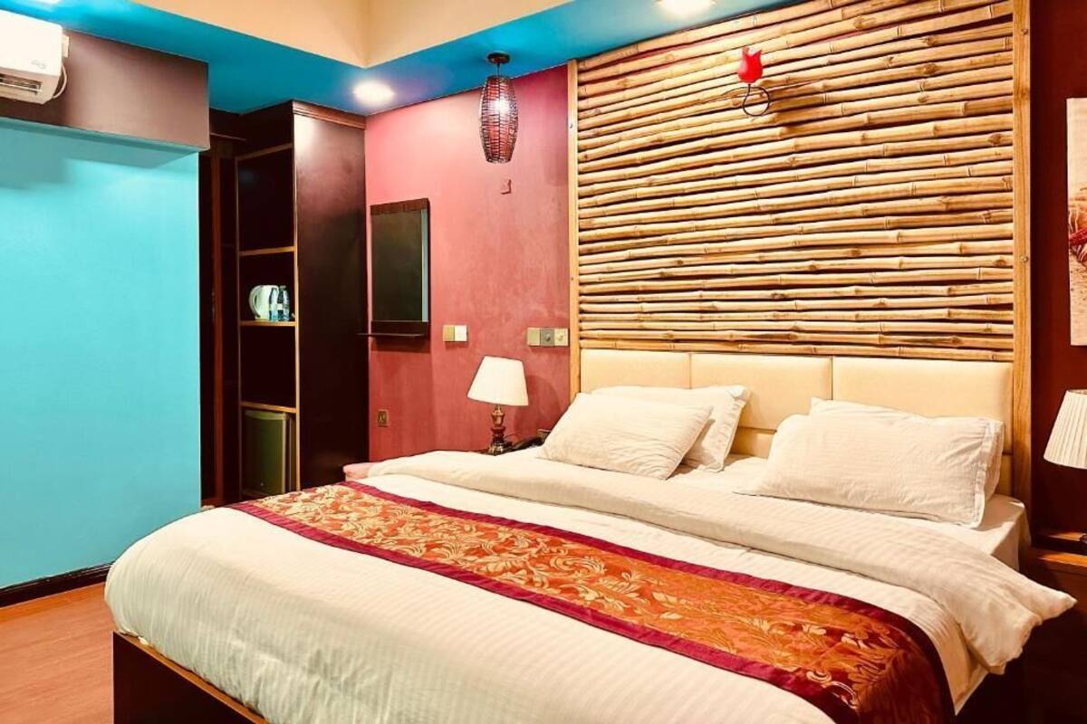 Una camera d'albergo con un letto, una parete rossa e una parete blu, e una testiera in bambù.