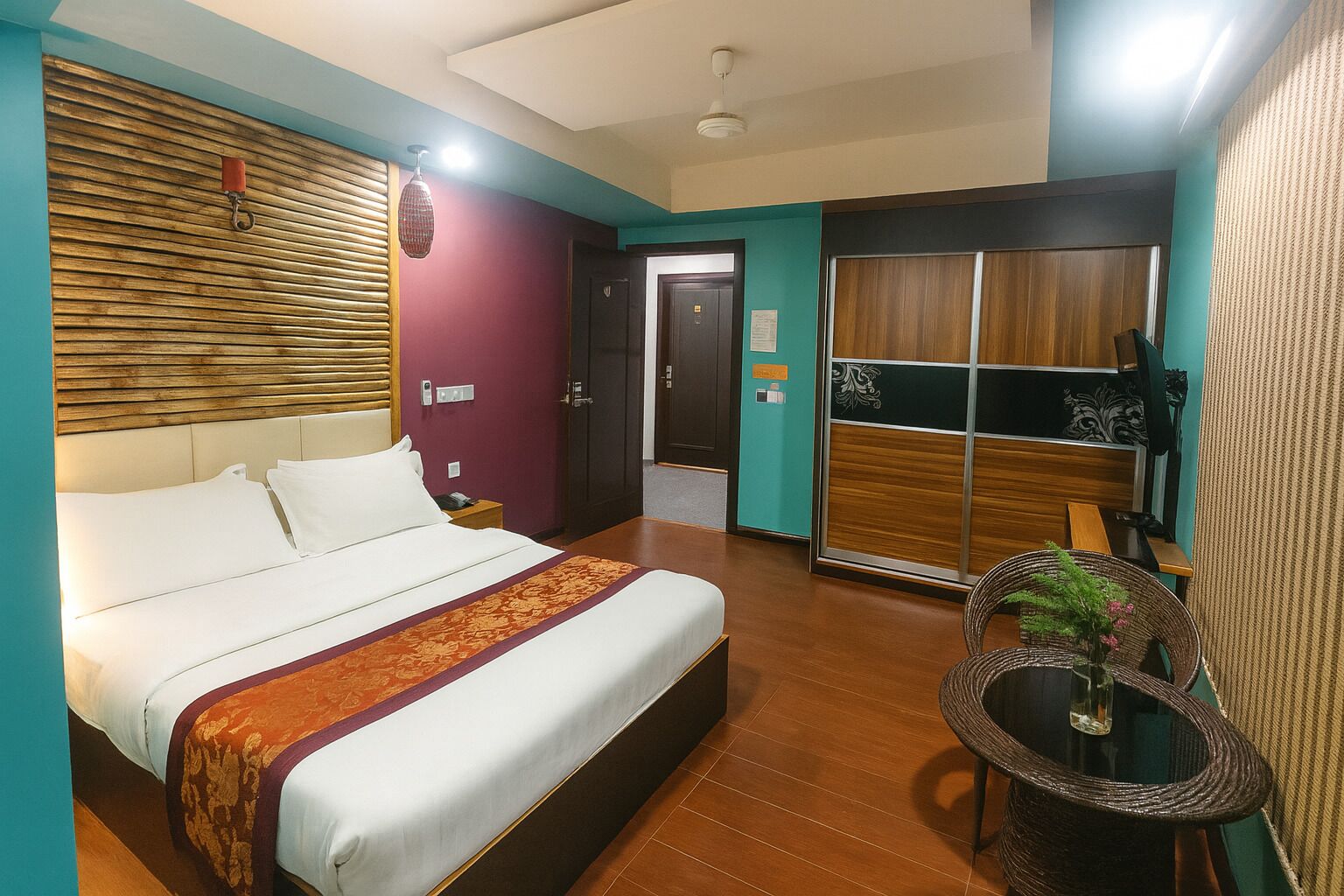 A hotel room with a bed, a small table with a plant, a mirror, and a wardrobe.