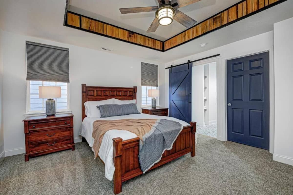 A bedroom with a wooden bed, two bedside tables, a ceiling fan, and a blue door.