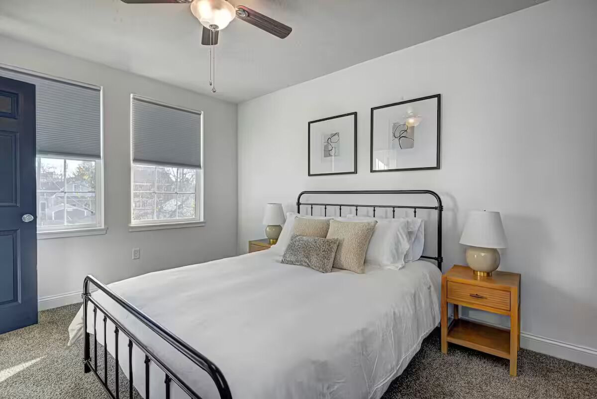 A bedroom with a bed, two bedside tables, a ceiling fan, and two framed pictures on the wall.