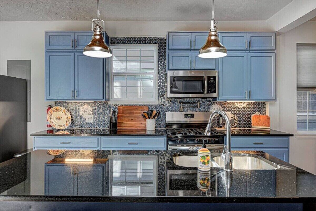 A modern kitchen with blue cabinets, a black countertop, and stainless steel appliances.