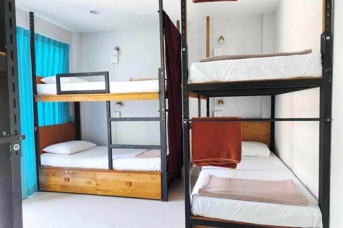A dormitory room with bunk beds, a wooden desk, and a small window with curtains.