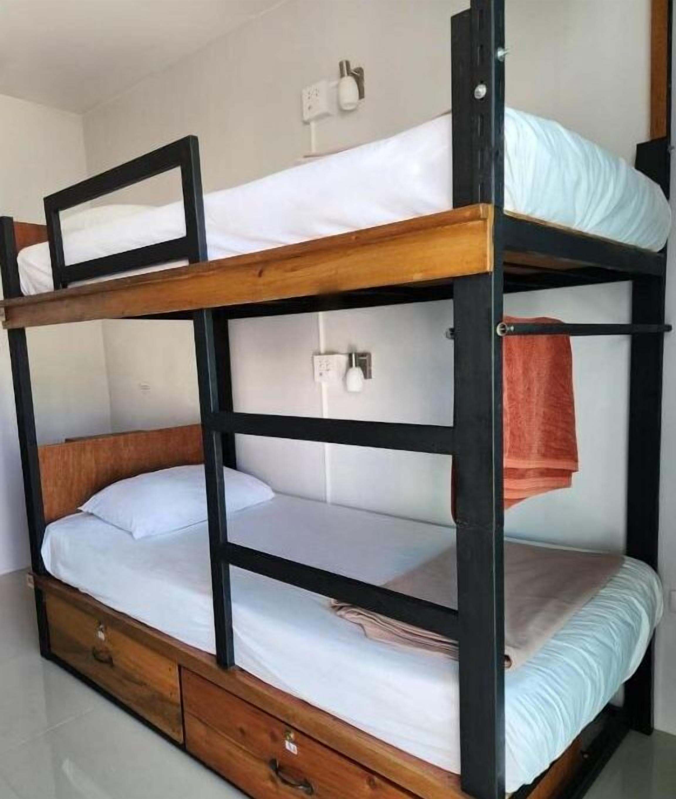 A bunk bed with a wooden frame, white bedding, and a small wooden drawer.