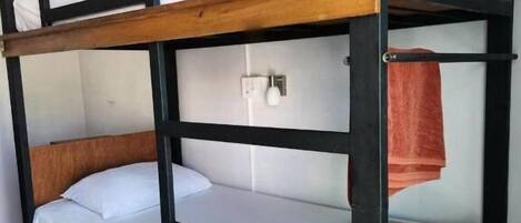 A bunk bed with a wooden frame, white bedding, and a small wooden drawer.