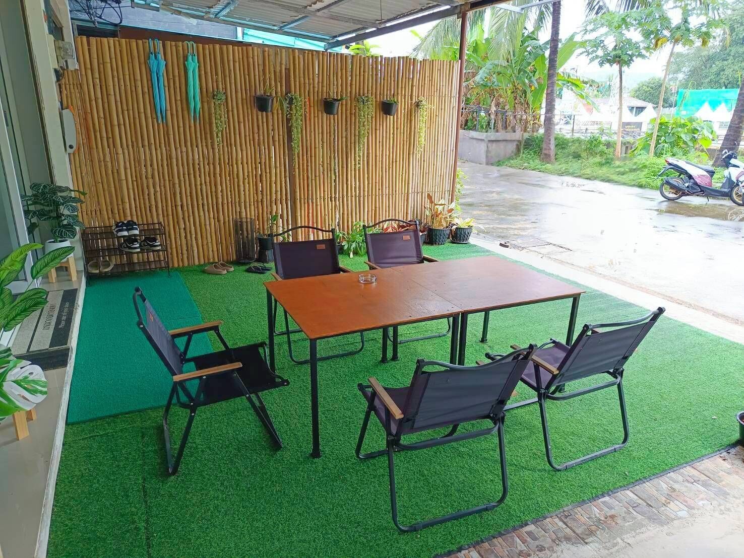 An outdoor seating area with a bamboo backdrop, green artificial turf, and a wooden table with chairs.