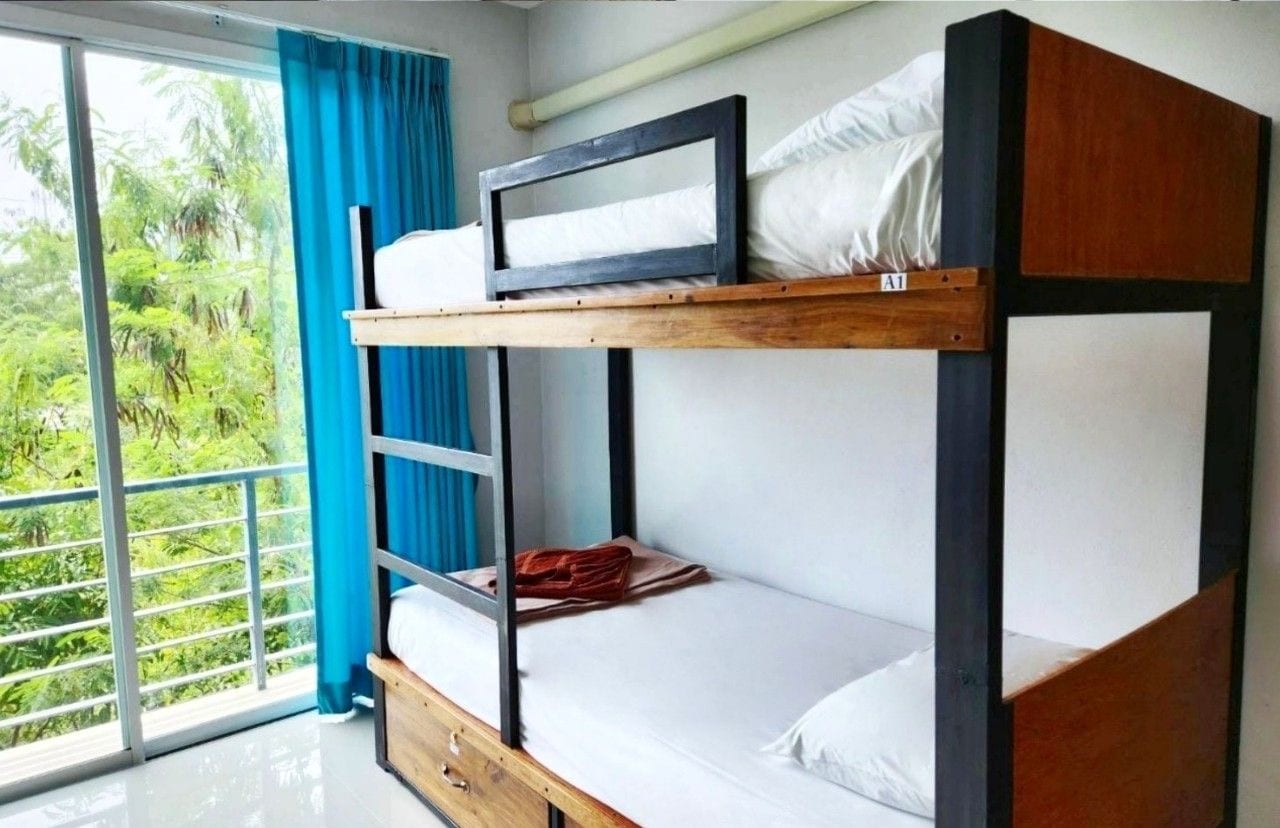 A 4-bed female dorm with bunk beds, a wooden frame, and a view of greenery through a large window.