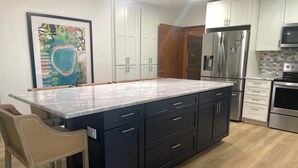 Une cuisine moderne dotée d’un grand îlot central, d’appareils électroménagers en acier inoxydable et d’une œuvre d’art encadrée accrochée au mur.