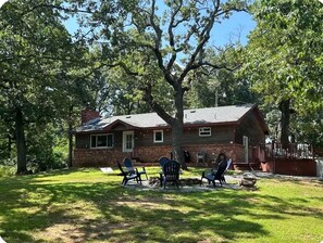 Casa com fachada de tijolos, chaminé e uma árvore na frente. Quatro cadeiras Adirondack estão dispostas no gramado.