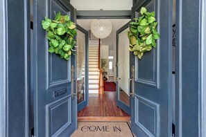 A hallway with dark blue doors, a 'COME IN' mat, and green foliage decorations. - The Regent on Whitaker | Downtown Savannah Luxury (Savannah)