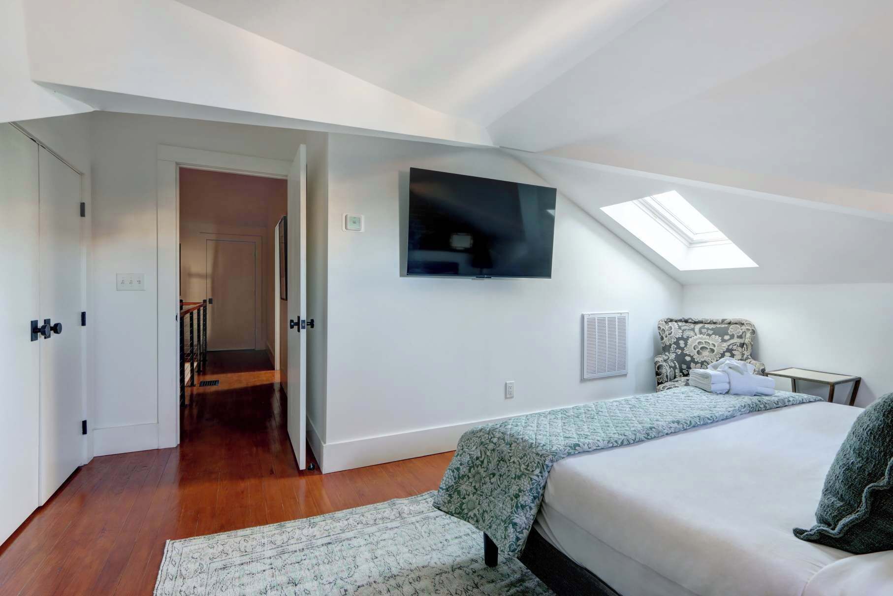 Un dormitorio con una cama, una silla, un televisor y un tragaluz.