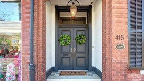 A brick building entrance with a dark gray double door, two green wreaths, a "COME IN" mat, and a number plaque reading "415". - The Regent on Whitaker | Downtown Savannah Luxury (Savannah)